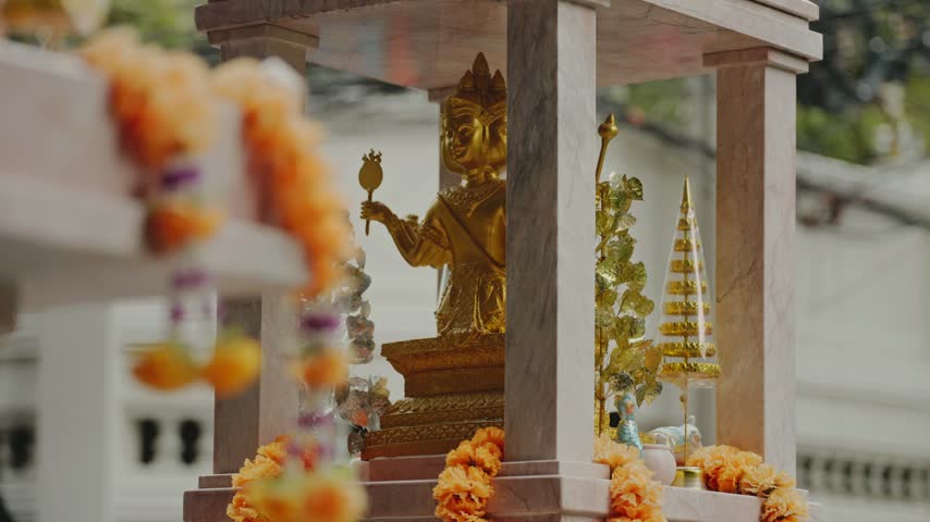 Phra phrom golden statue in a spirit house with flower offerings on a street in bangkok