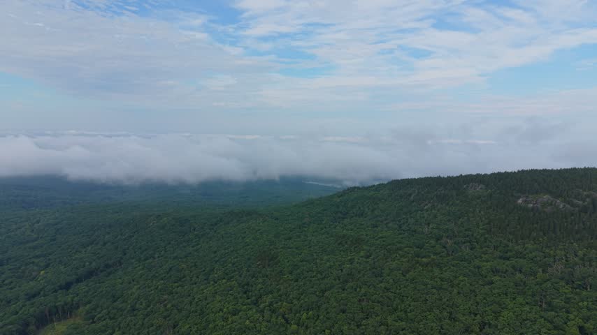 Low hanging clouds and fog over the lush green forested slopes of Mount Monadnock in New Hampshire. Aerial forward