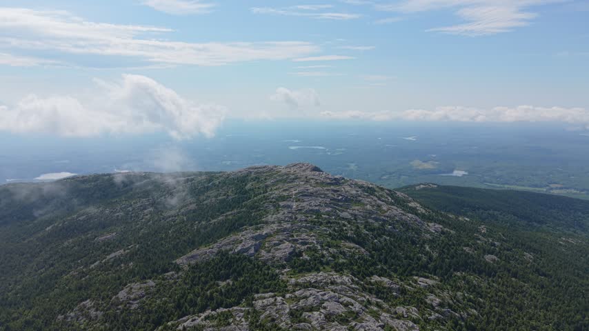Mount Monadnock’s rocky summit ridge stretches above dense green forest under a bright summer sky captured from above, Monadnock State Park, New Hampshire, US