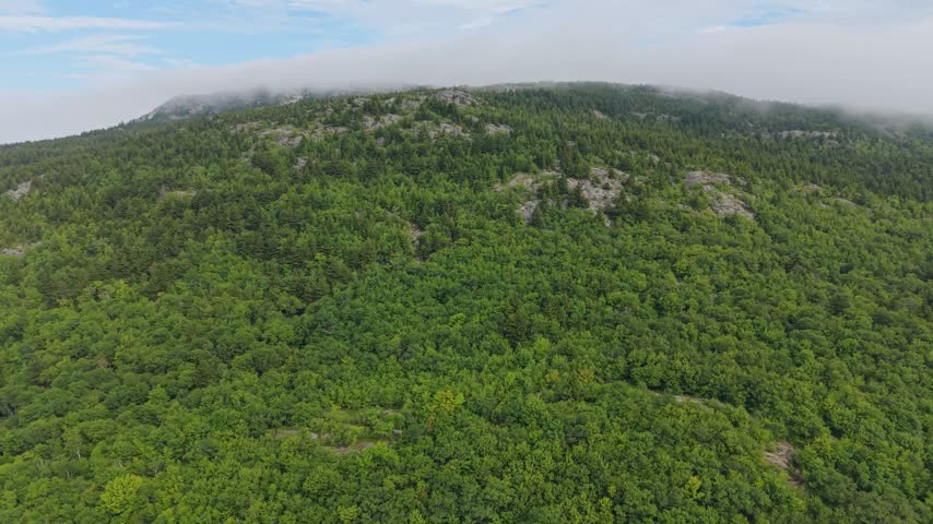 Low clouds skim the tree covered slopes of Mount Monadnock as the wide aerial pass reveals the surrounding New Hampshire woodland, Monadnock State Park, US