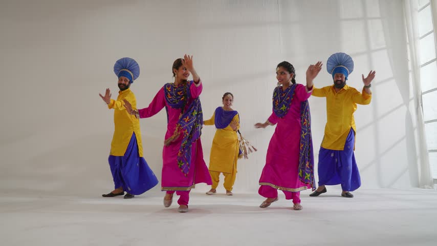 Group of Indian performers are energetically dancing Bhangra in a studio setting