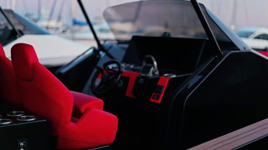 Luxurious motorboat helm station featuring sleek black dashboard design and bright red leather captain seat in marina harbor.