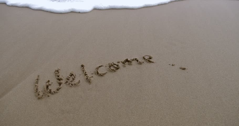 Sandy beach scene featuring word Welcome written in sand with waves softly washing over it.