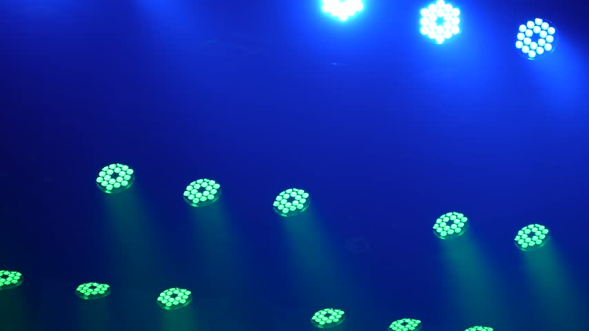 cinematic panning shot of bright blue and green led stage lights emitting light beams through smoke in a dark concert or nightclub venue