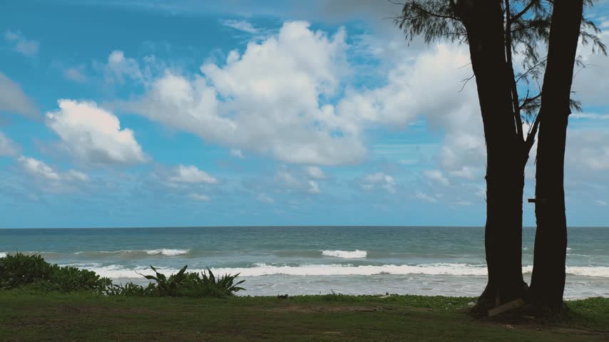 A serene tropical beach in Thailand featuring gentle ocean waves, a sandy shore, and a bright blue sky with clouds.