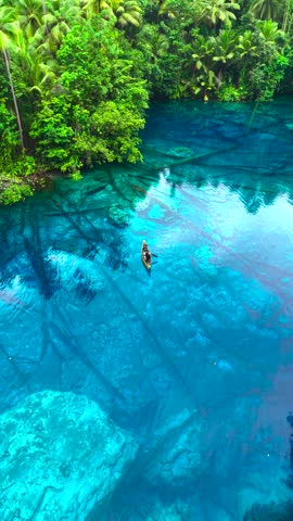 Aerial view of a man and a woman paddling a wooden canoe over submerged trees in clear blue water at Paisupok Lake, Banggai, Sulawesi, Indonesia.