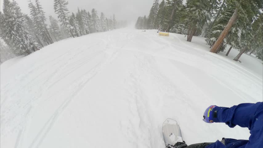 Snowboarder riding through heavy wet snow at Northstar California ski resort in Lake Tahoe, surrounded by snow-covered mountain terrain and winter forest.