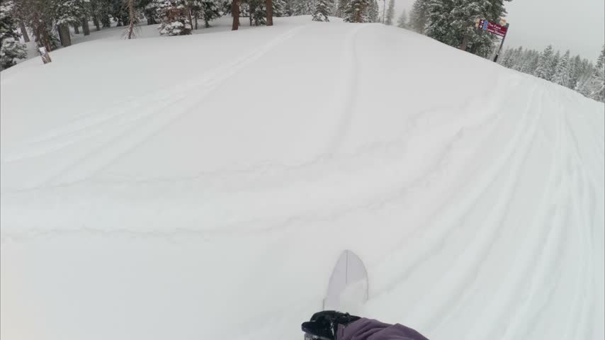 Snowboarder riding through fresh powder at Northstar California ski resort in Lake Tahoe, surrounded by snow-covered mountain terrain and winter forest looking down