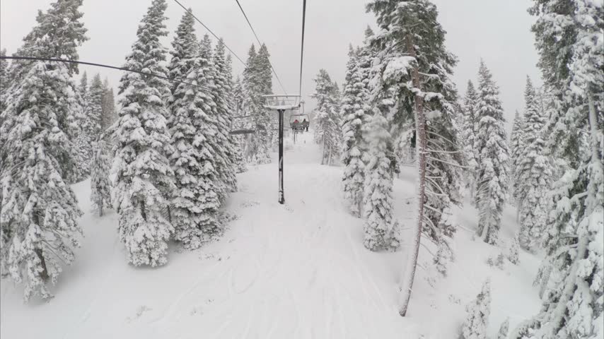 View from a ski lift in snowy conditions at Northstar California ski resort as a snowboarder rides down the mountain below through a winter landscape.