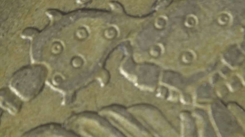 Close up spinning shot of a Mexican coin showing an eagle holding a snake on its surface. Detailed engraving highlights the symbolic design and metallic texture.