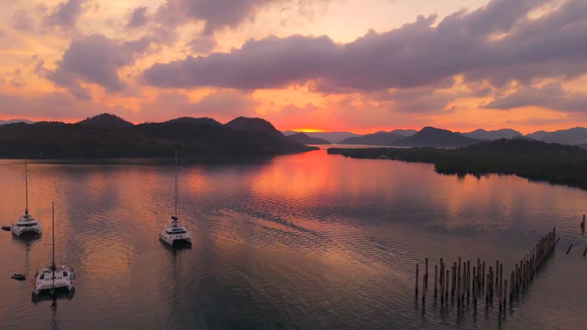 Aerial panorama of orange sunset reflections over a quiet Coron bay with boats and old wooden pilings