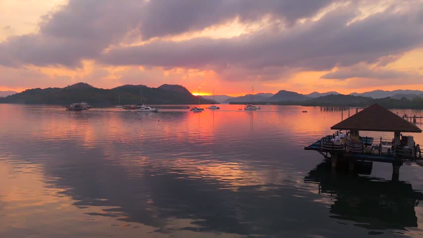 Sunset view across a quiet Coron bay with anchored boats and a waterside pavilion beside a wooden jetty
