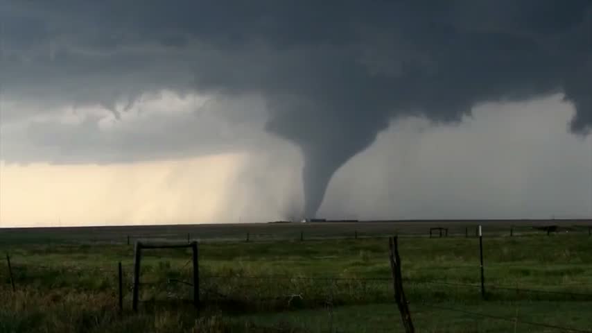 Powerful tornado twisting in a stormy sky over a rural landscape with a fence