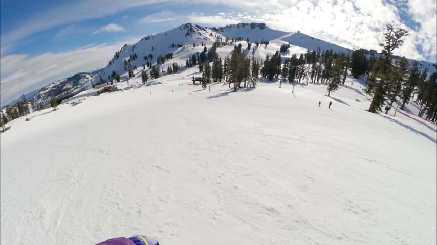 First-person POV of snowboarding down a groomed ski run at Palisades Tahoe on a sunny day, with scenic mountain terrain surrounding the resort.