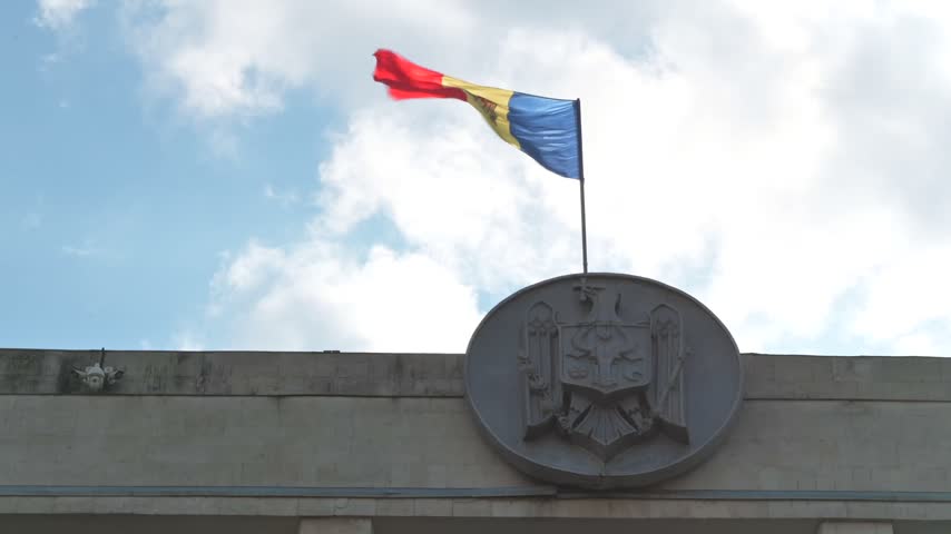 Moldovan flag fluttering against bright sky over official state building facade in Chisinau.