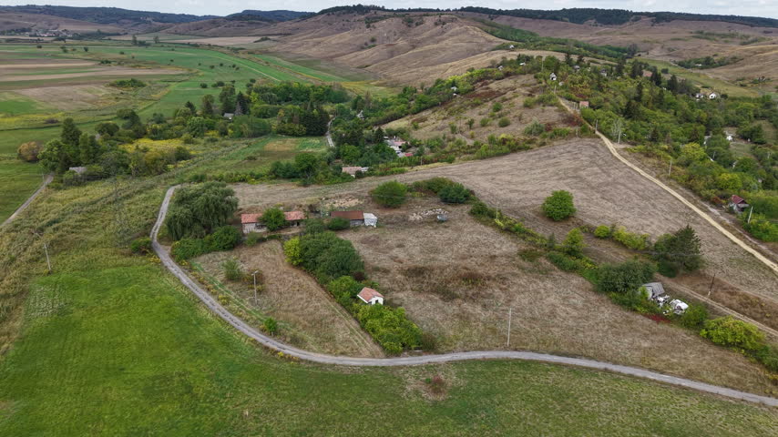 An aerial view captures a serene rural landscape with rolling hills, varied fields, and winding paths connecting scattered farmsteads.