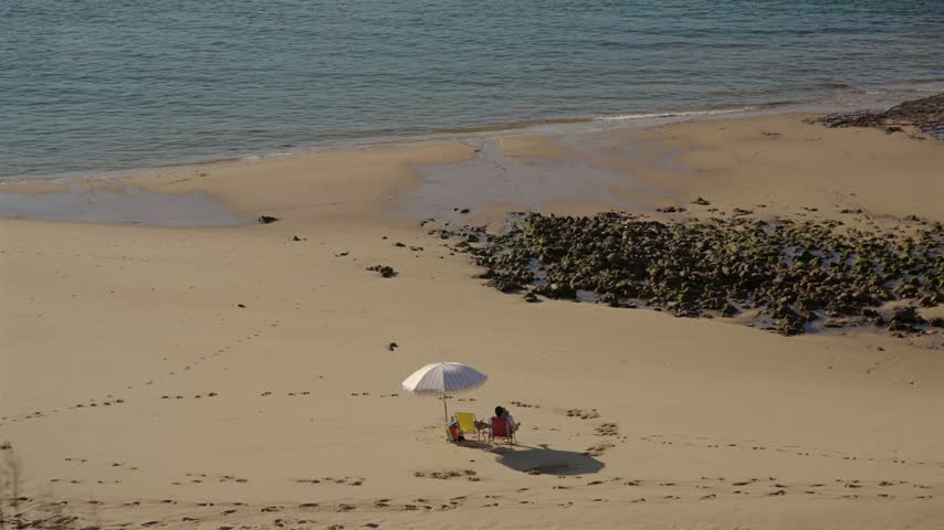 Couple relaxing under a beach umbrella on an empty sandy beach, Alentejo, Portugal