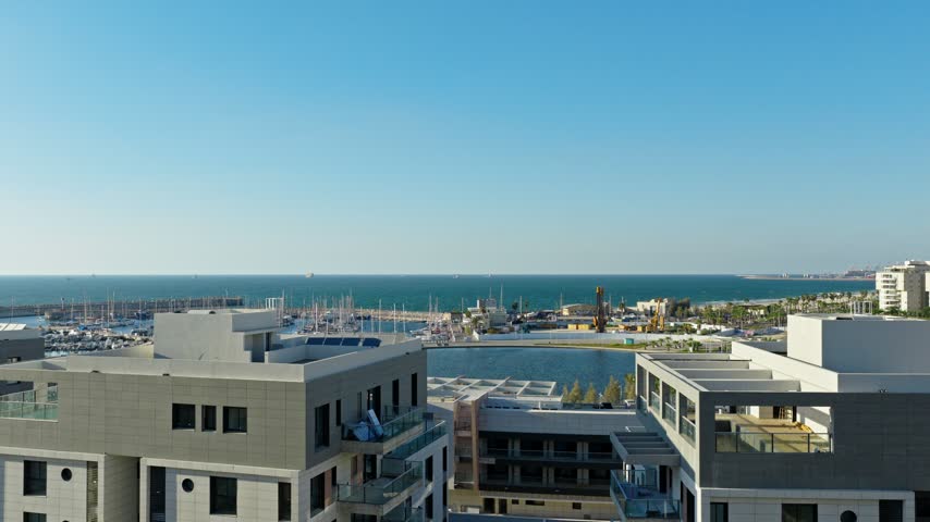Aerial drone shot of Ashdod marina with yachts, circular artificial lake, coastline, and blue Mediterranean Sea under a clear sky in Israel.