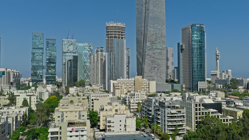 Aerial drone view over residential roofs toward the Sarona Tower, Azrieli Town, and modern high tech skyscraper skyline in Tel Aviv Israel.