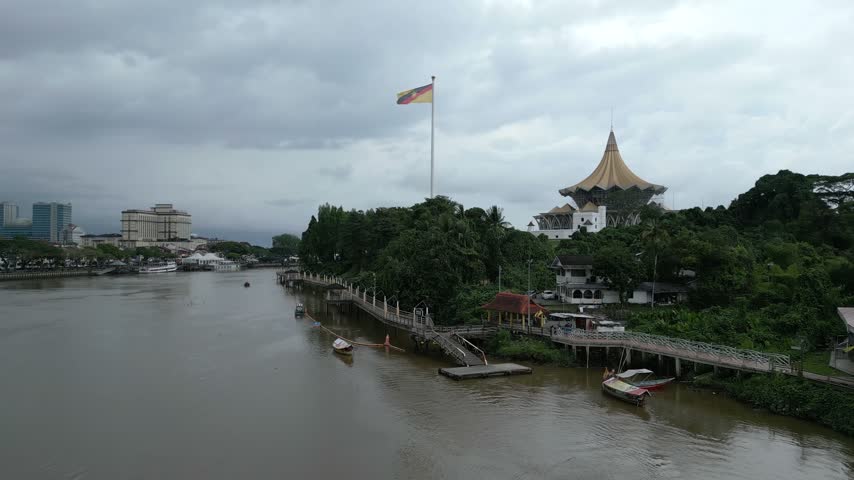 Aerial view of the Sarawak State Legislative Assembly Building along the Sarawak River with a pedestrian walkway and lush greenery in Kuching, Sarawak, Malaysia.