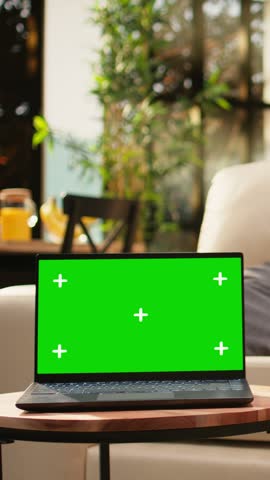 Portrait format: Green screen mockup appears on a laptop on a wooden coffee table in an empty modern living room with cozy rustic decor and stylish open space