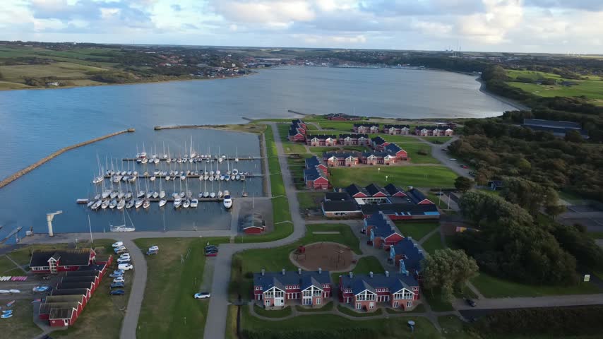 Wide drone shot of a marina filled with sailboats, stone breakwater and a large coastal bay in Denmark. Calm Scandinavian waterfront scenery.