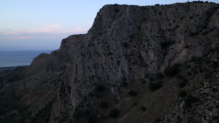 Aerial view of rugged limestone cliffs overlooking the Mediterranean Sea at dusk in Terrasini, Sicily, Italy.