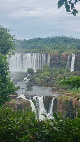 Vertical shot of Iguazu Falls from Brazil, looking across the border toward Argentina, with roaring cascades, misty waters and dense tropical rainforest surrounding the iconic natural landmark