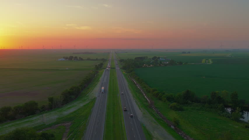 Diesel freight rolls down an old interstate while a new generation of turbines turns on the horizon — the heartland