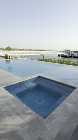 A serene infinity pool edge overlooking a tranquil lake with a distant pier and boat in bright daylight.