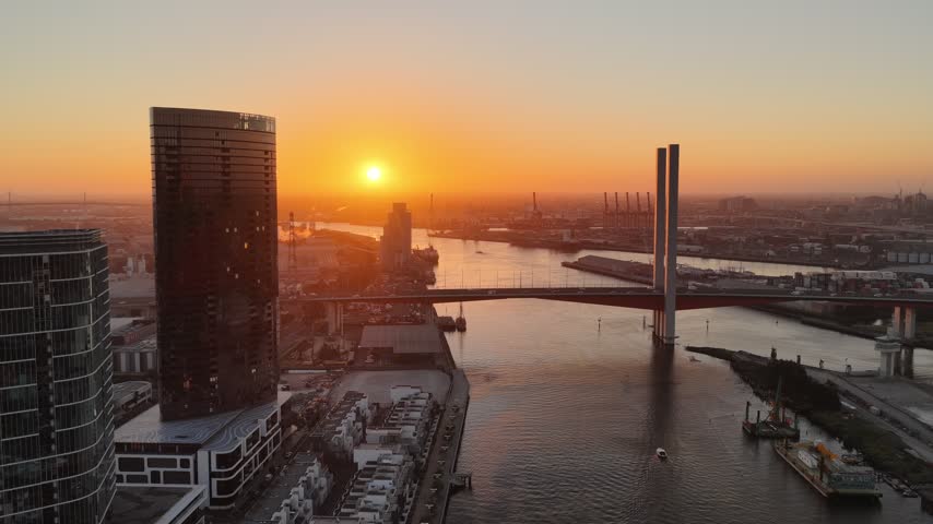 Port Melbourne, Victoria, Australia – 4K aerial drone view of Bolte Bridge over Yarra River, CBD skylines, Port of Melbourne container terminal, industrial waterfront at golden sunset