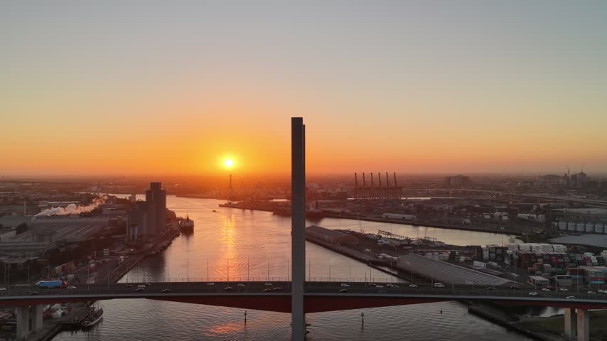 Port Melbourne, Victoria, Australia – 4K aerial drone view of Bolte Bridge over Yarra River, CBD skylines, Port of Melbourne container terminal, industrial waterfront at golden sunset