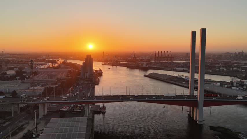 Port Melbourne, Victoria, Australia – 4K aerial drone view of Bolte Bridge over Yarra River, CBD skylines, Port of Melbourne container terminal, industrial waterfront at golden sunset