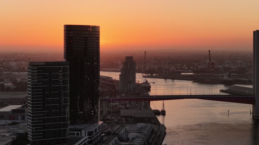 Port Melbourne, Victoria, Australia – 4K aerial drone view of Bolte Bridge over Yarra River, CBD skylines, Port of Melbourne container terminal, industrial waterfront at golden sunset