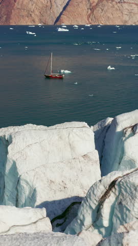 Sailboat Anchored In Open Polar Fjord Waters Near Glacial Ice In Scoresby Sund Greenland. - aerial vertical shot