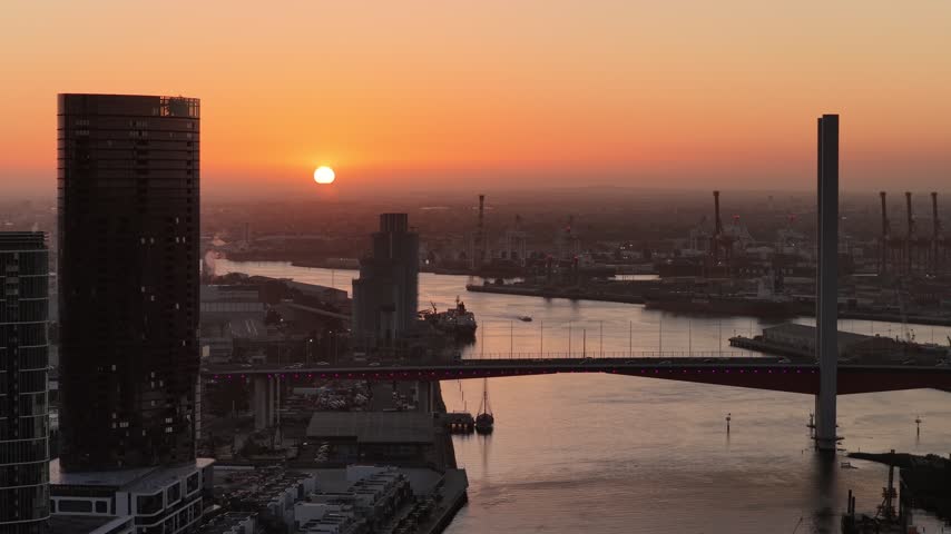 Port Melbourne, Victoria, Australia – 4K aerial drone view of Bolte Bridge over Yarra River, CBD skylines, Port of Melbourne container terminal, industrial waterfront at golden sunset
