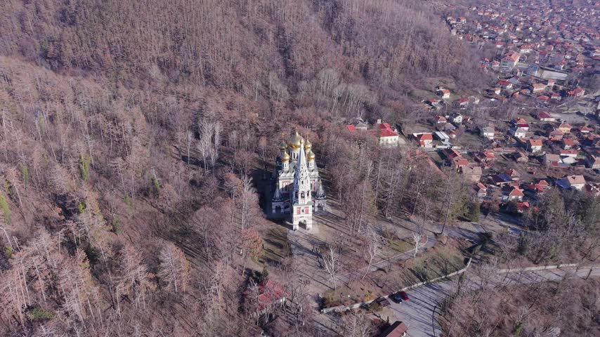 Aerial view of the Shipka Memorial Church with its golden domes and white facade surrounded by dense forest in Shipka, Stara Zagora, Bulgaria.