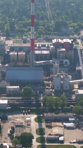 High angle view of a bulldozer moving coal in a large storage pile at a power plant. Industrial machinery and railway tracks nearby