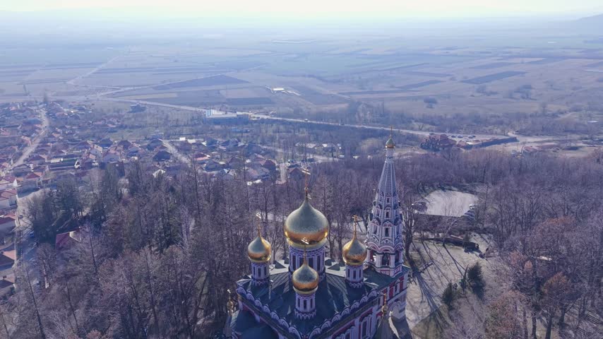 Aerial view of the ornate Shipka Memorial Church with its golden domes rising above the surrounding forest and the town of Shipka, Stara Zagora, Bulgaria.