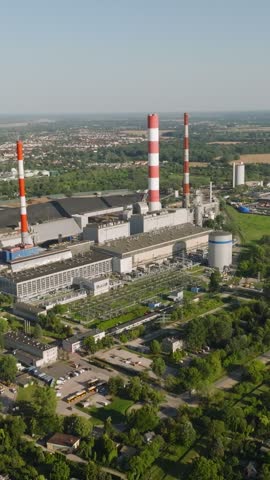 Panoramic aerial view of a coal fired power plant with towering red and white striped chimneys located on the outskirts of a city