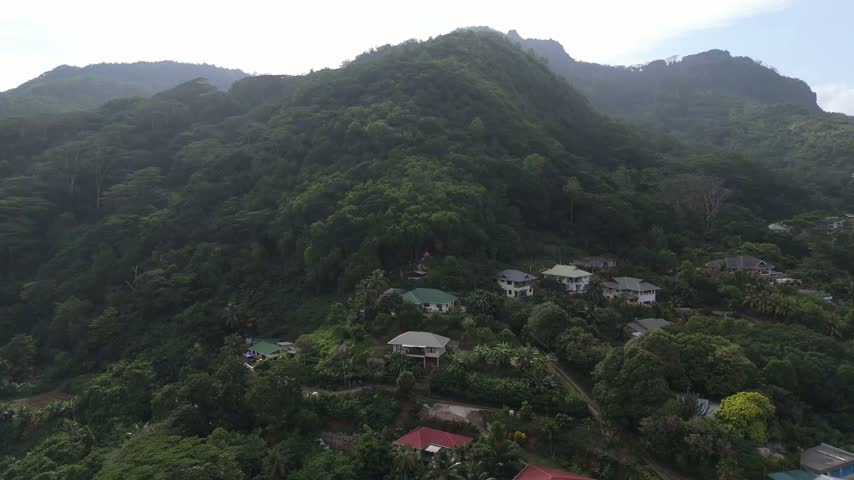 Aerial view of Mahe mountainside with scattered houses nestled in lush tropical vegetation under a cloudy sky in Seychelles.