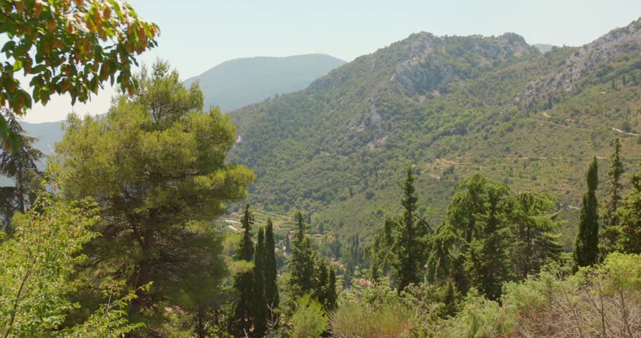 Panoramic view of a mountainous landscape on the French Riviera, featuring forested slopes, rocky peaks, pine trees and Mediterranean vegetation under a clear summer sky.