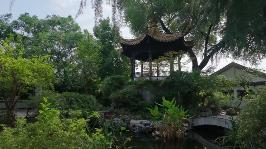 Nanjing, China - September 25th 2026 - Photo of traditional Chinese pavilion standing on a stone terrace above a garden pond with rockery and aquatic plants.