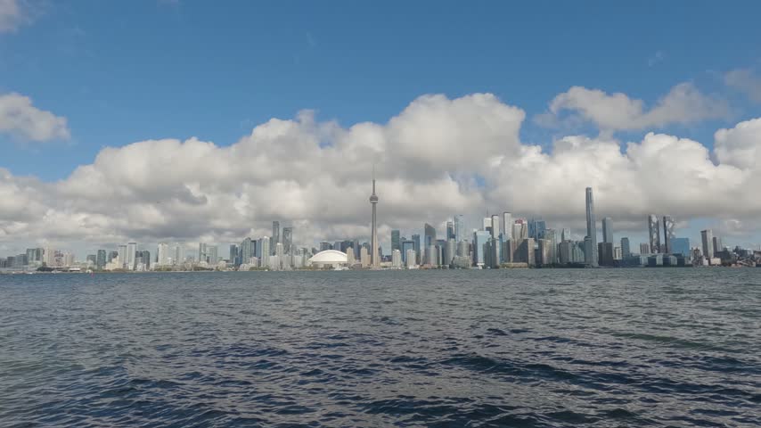 Wide timelapse of Toronto skyline from Centre Island as clouds sweep across the city and a ferry approaches over Lake Ontario.