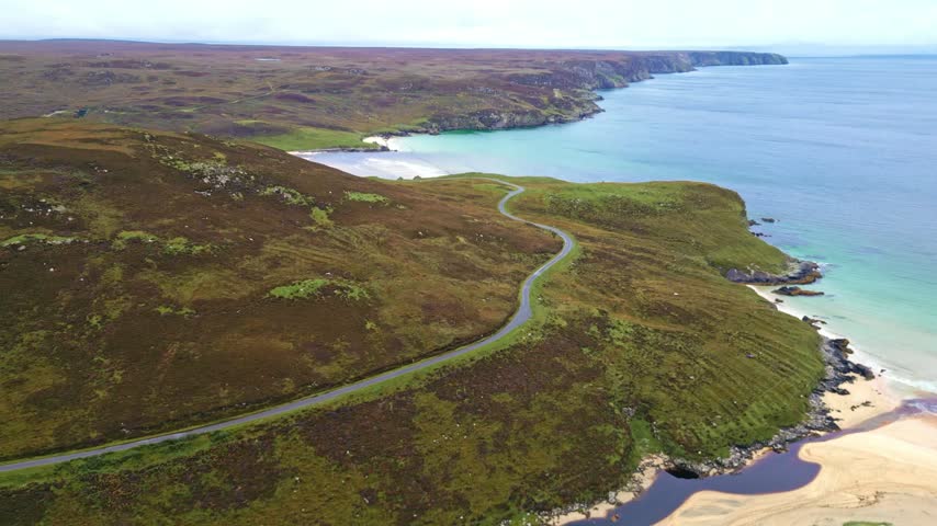 Aerial view of winding coastal road, sandy beach, and rugged shoreline in Scotland