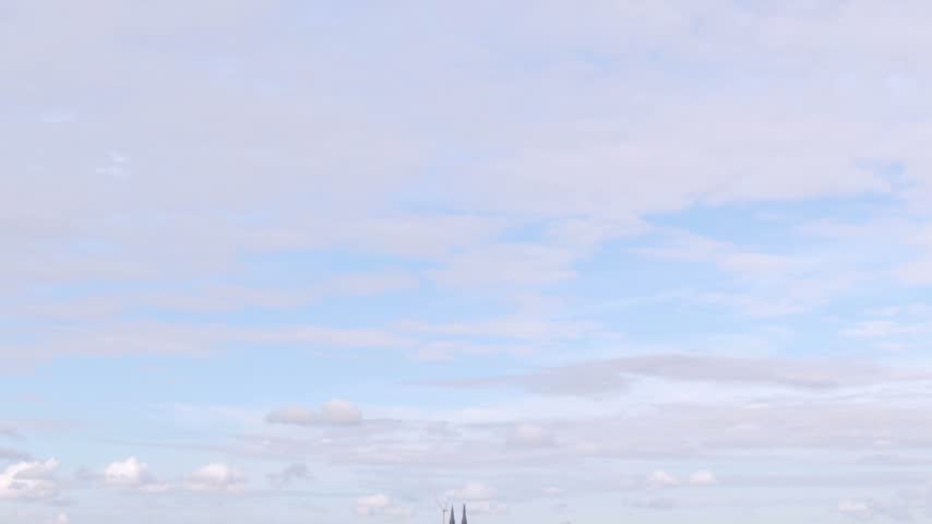 Wide aerial of Uppsala skyline under soft clouds: pink castle left, twin cathedral spires and cranes along the horizon.