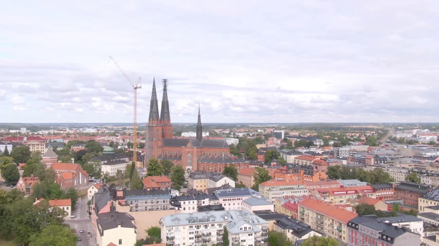 Aerial Uppsala cathedral red-brick twin spires with yellow crane, scaffolding, Gothic roofs and trees.