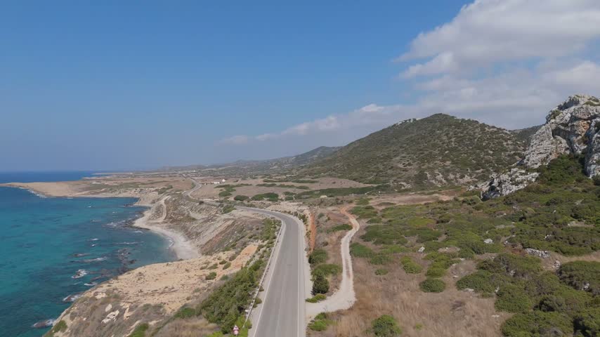 Aerial view of a winding coastal road along the Mediterranean Sea with rocky cliffs and scrubland in Famagusta, Famagusta, Northern Cyprus.