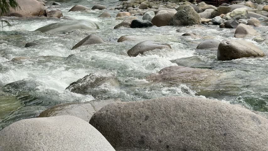 White water rapids rushing over smooth granite boulders in a mountain river at Lynn Canyon in Vancouver, showing turbulent flowing water and rocky riverbed.