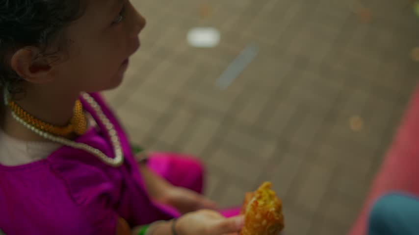 Children in colorful clothes eat snacks while sitting on outdoor plastic chairs